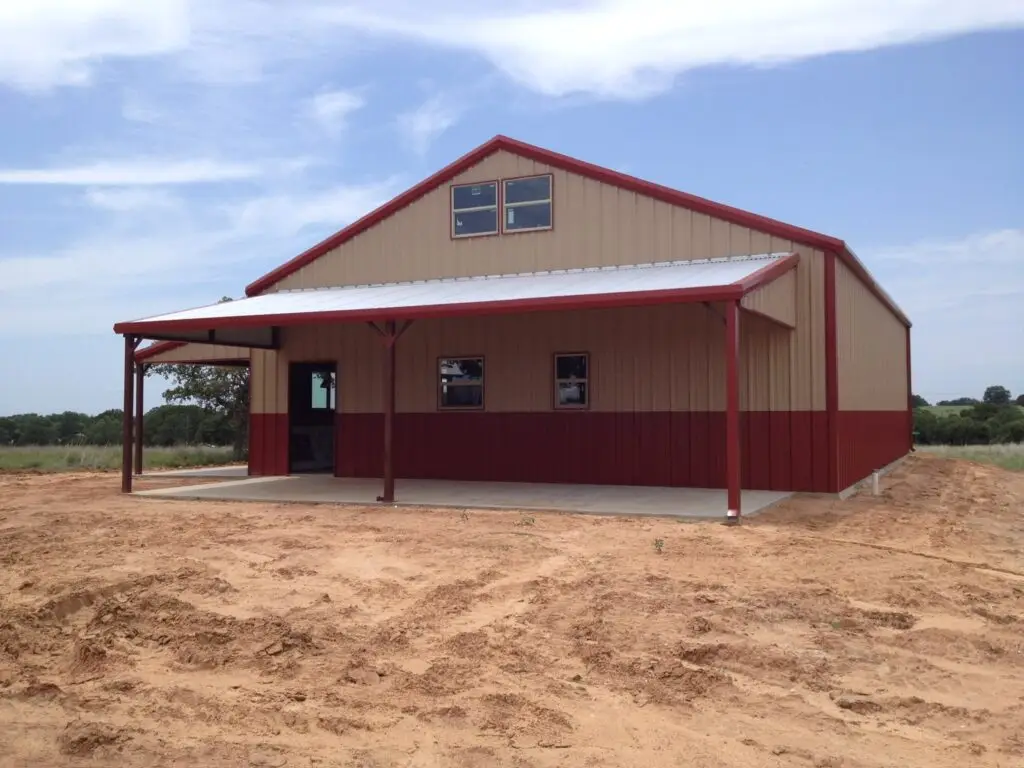 A red and tan barndo with a porch that has a white roof. There are windows installed but no doors.
