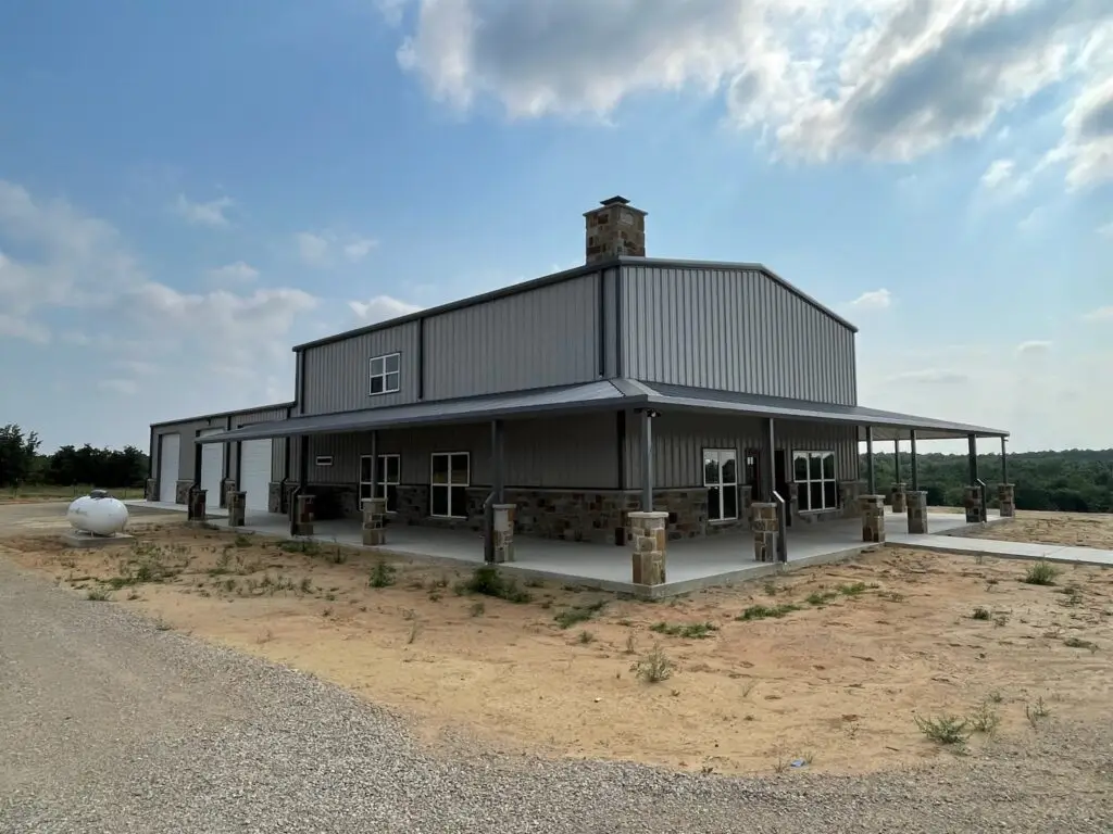 Tall tan barndominium with a chimney and large wraparound porch